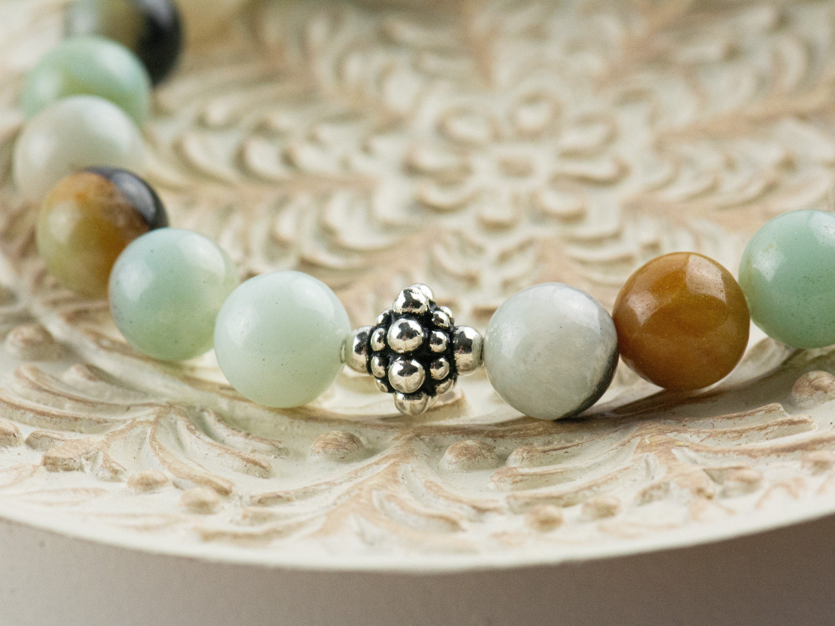 Black Gold Amazonite Genuine Gemstone Stretch Bracelet displayed on a decorative bowl. Amazonite beads are multicolor earth-tones. Close up of center bead is a silver Bali style bead.