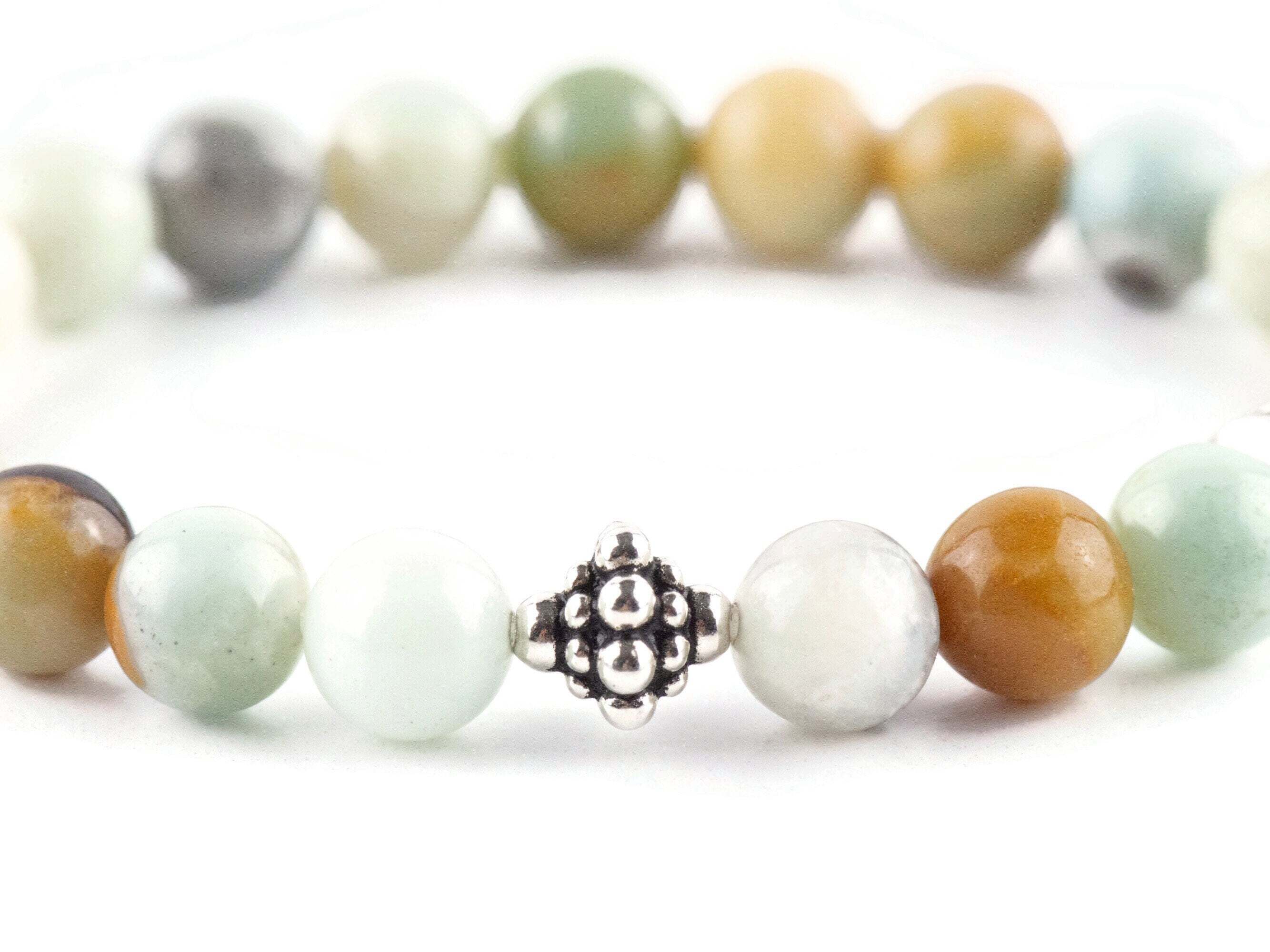 Black Gold Amazonite Genuine Gemstone Stretch Bracelet on white background. Amazonite beads are multicolor earth-tones. Close up of center bead is a silver Bali style bead.