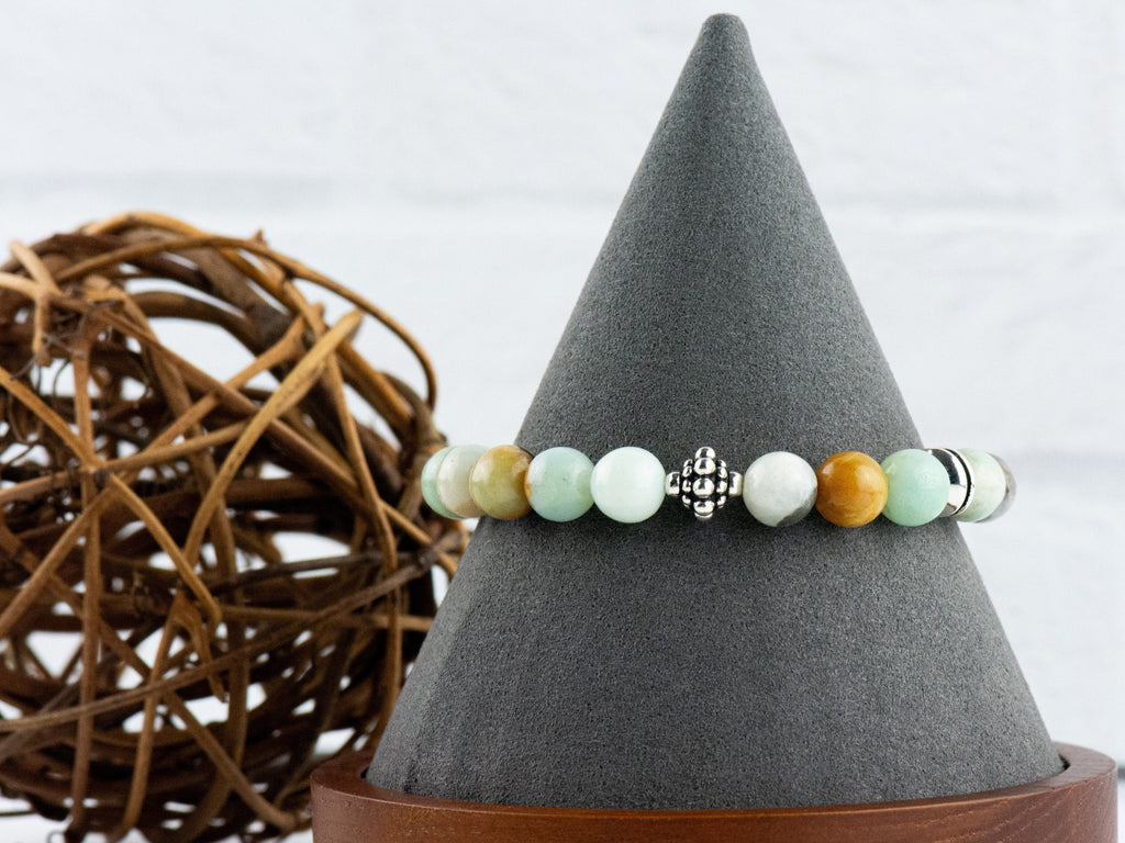Black Gold Amazonite Genuine Gemstone Stretch Bracelet displayed on a decorative black bracelet stand. Amazonite beads are multicolor earth-tones. Center bead is a silver Bali style bead.