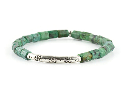 African Turquoise Stretch Bracelet on white background. Beads are bluish green with black and brown speckle. Silver pewter tube focal bead is adorned with floral etchings.