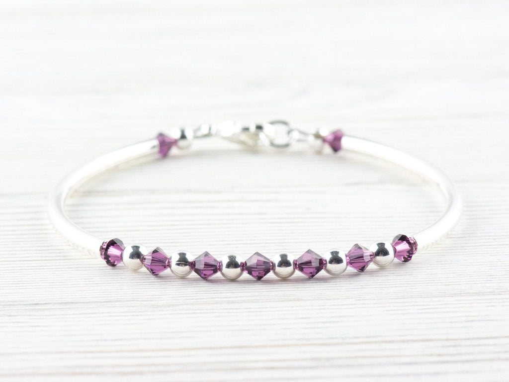 May include: A silver bangle bracelet with a row of small, dark purple crystals and silver beads.