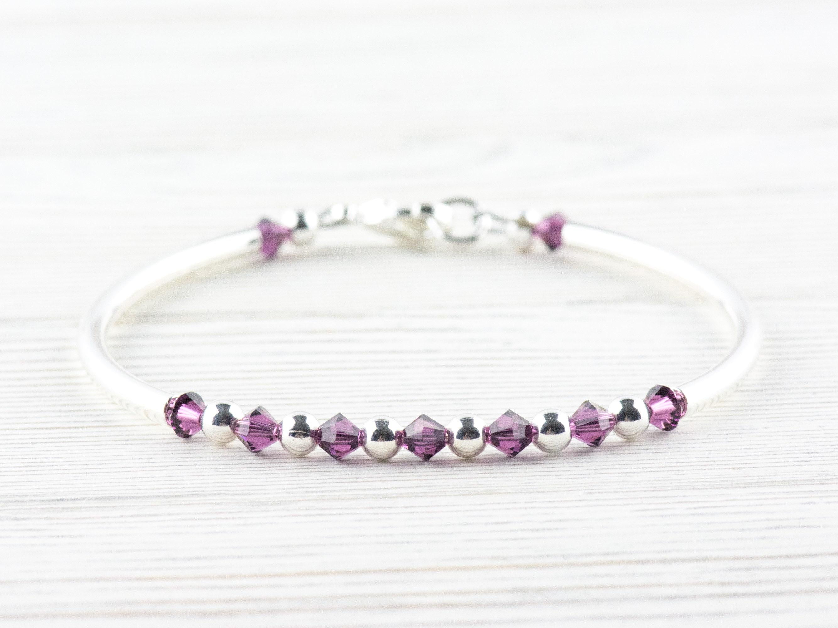 May include: A silver bangle bracelet with a row of small, dark purple crystals and silver beads.