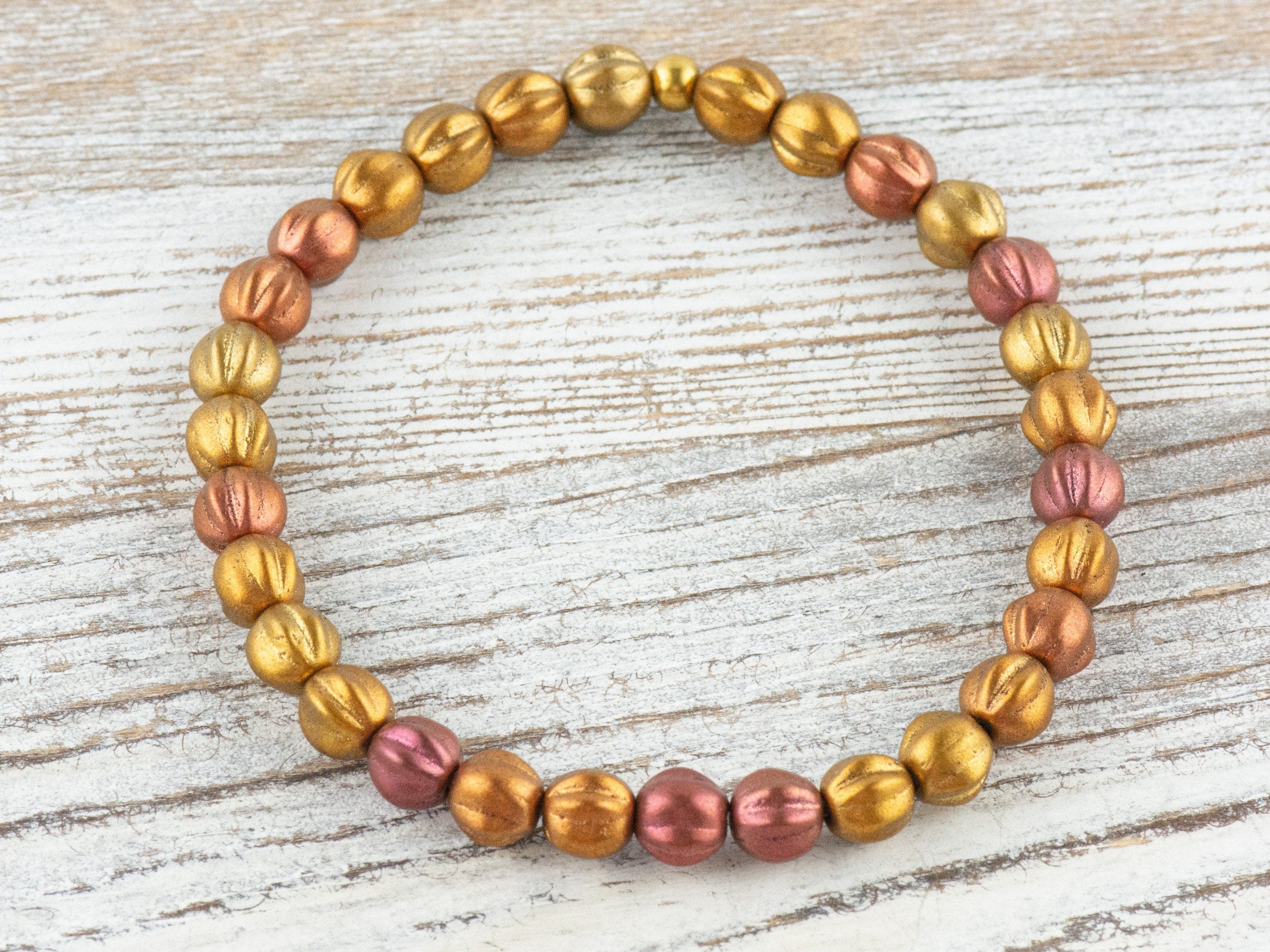 May include: A gold and rose gold beaded bracelet with a textured finish. The beads are round and have a slightly raised design.